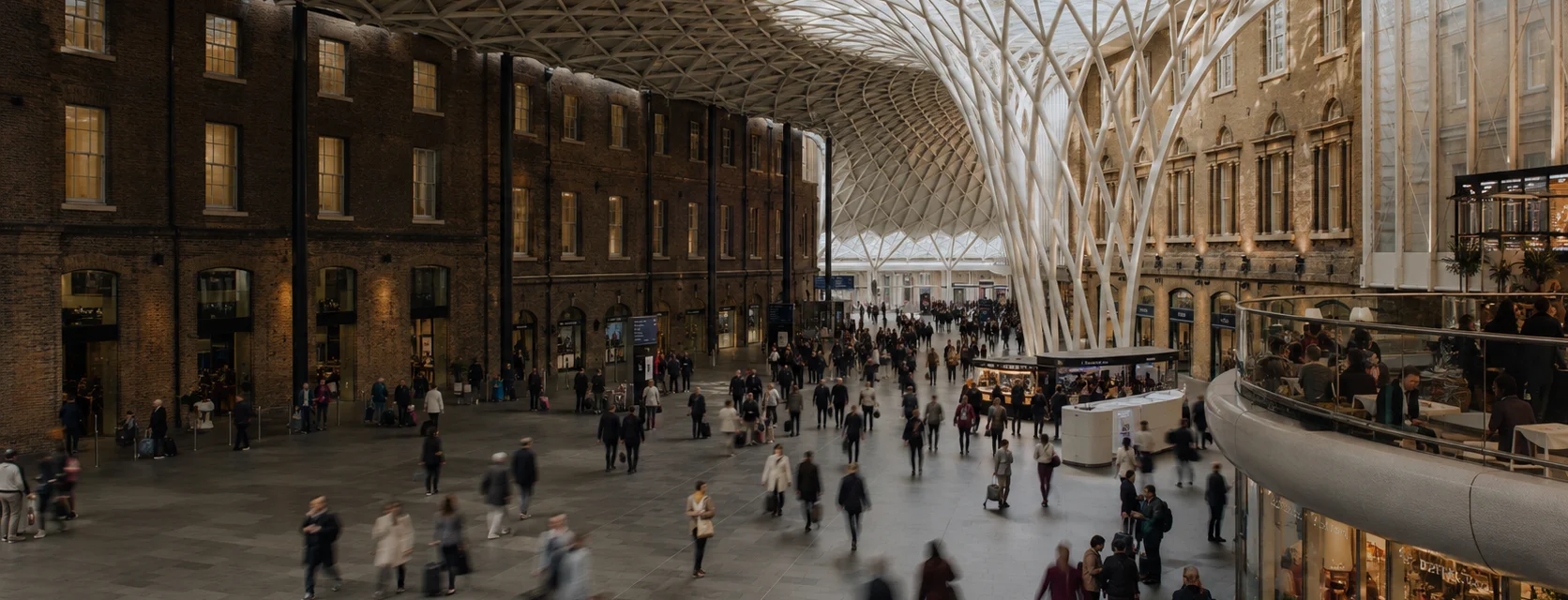 Illustrative station concourse with softly blurred commuters beneath a sweeping roof